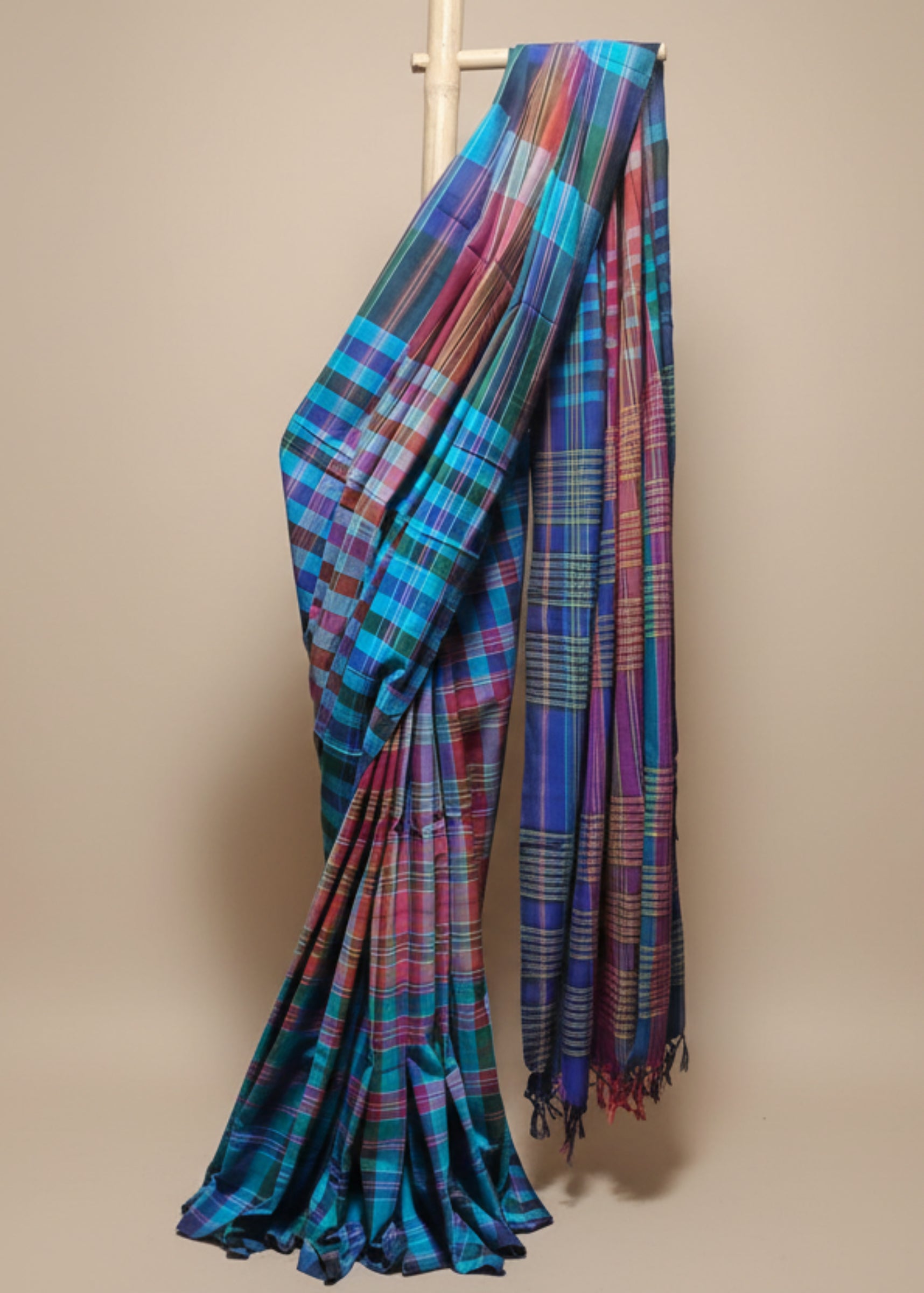 Multicolored plaid fabric draped over a wooden rod against a white curtain background