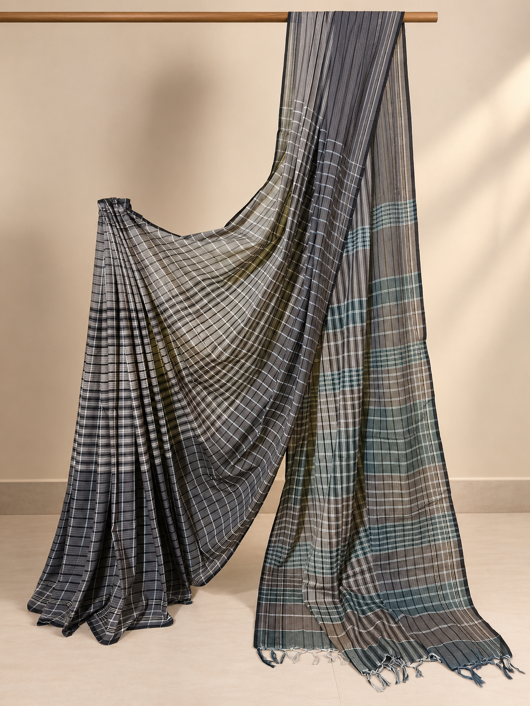 Charcoal grey and olive green handloom Gamchha saree with fine checks and stripes, contrasting checked pallu and handcrafted tassels displayed in a minimalist studio setting.