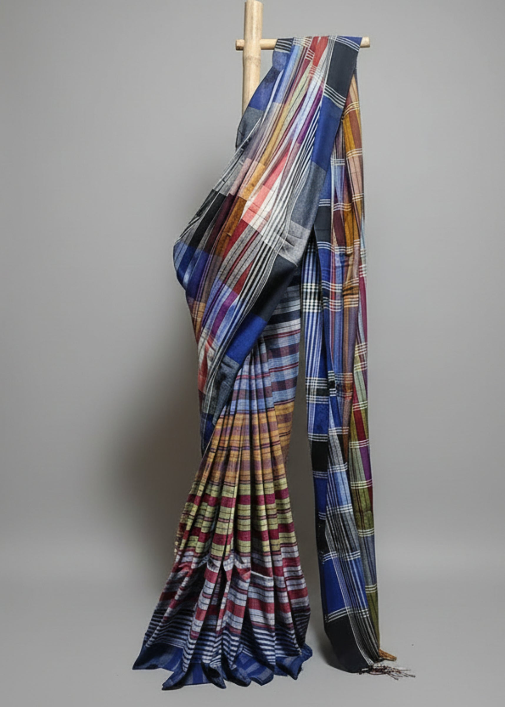 Colorful plaid saree draped over a wooden rod against a white curtain background