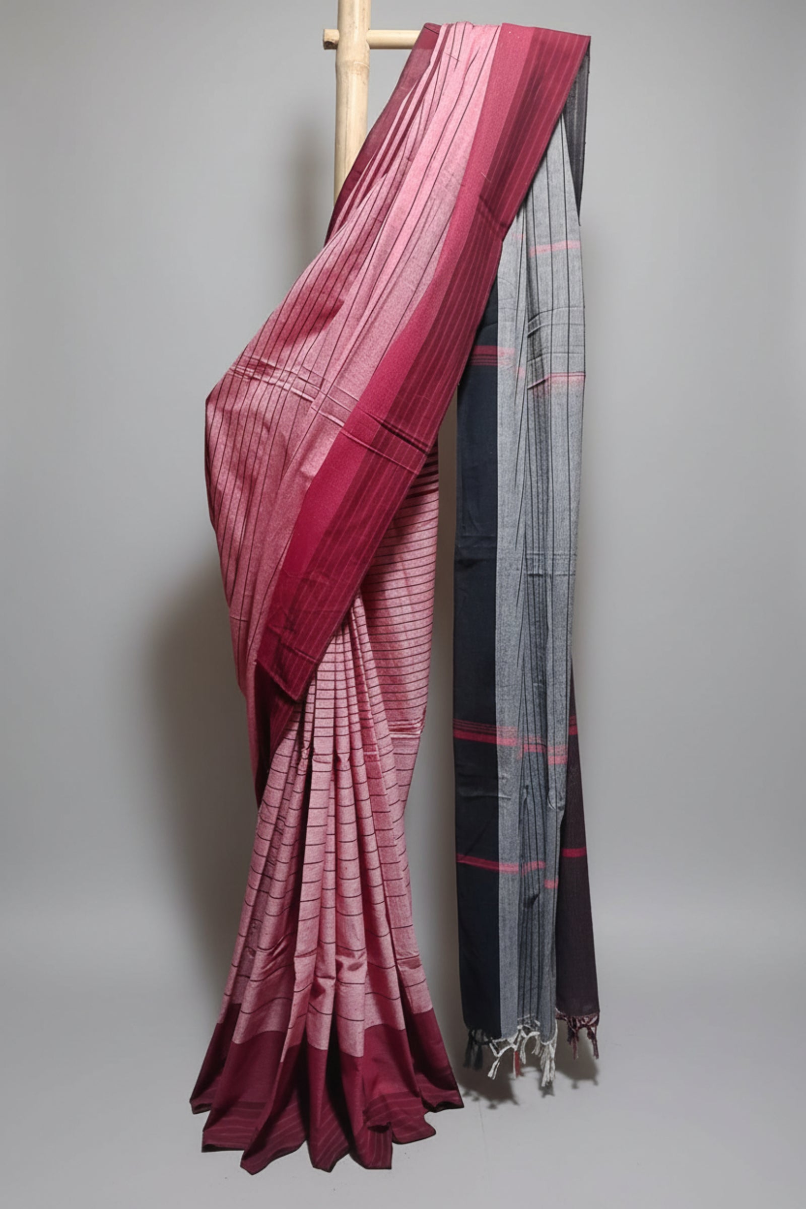 Saree with a maroon and white checkered pattern draped over a wooden rod against a white curtain background.
