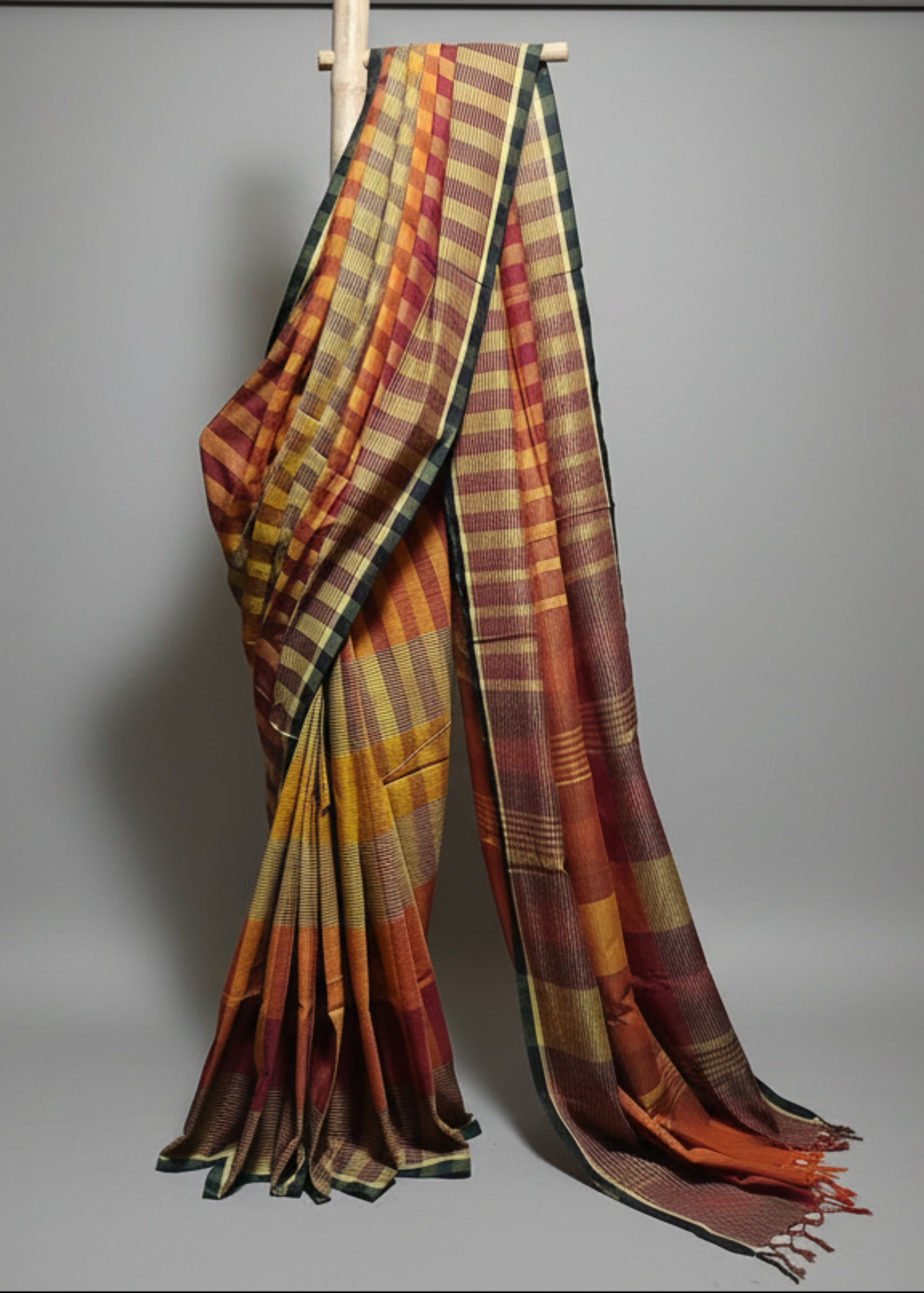 Plaid patterned saree draped over a wooden rod against a white background