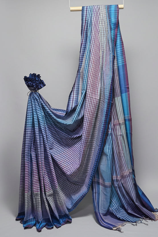 Blue and white checkered saree draped over a stick against a white curtain background