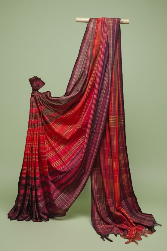 Red and purple plaid saree draped over a wooden rod against a white background