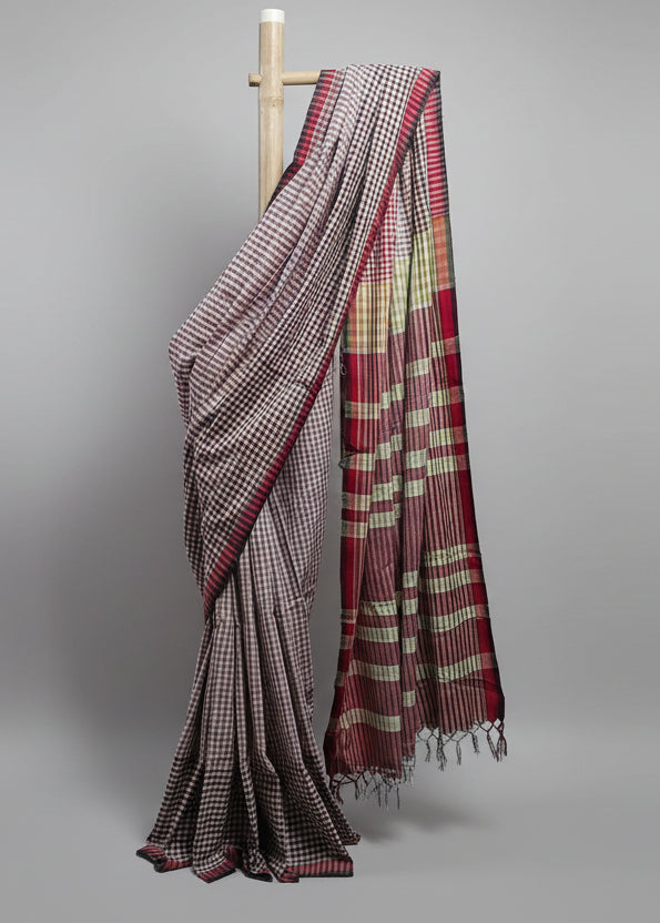 Checkered saree draped over a wooden rod against a white curtain background