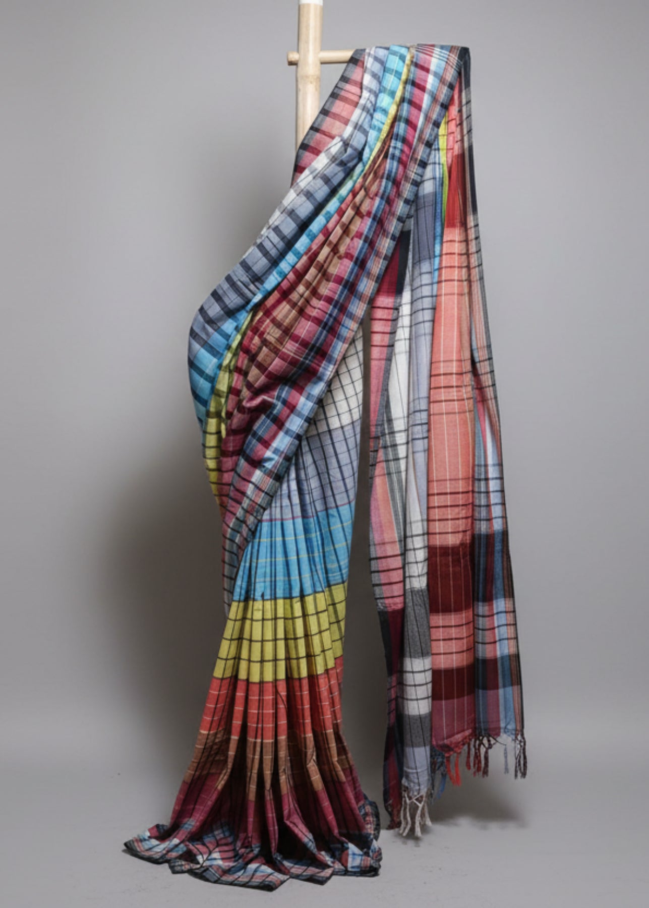 Multicolored plaid fabric draped over a wooden rod against a plain background